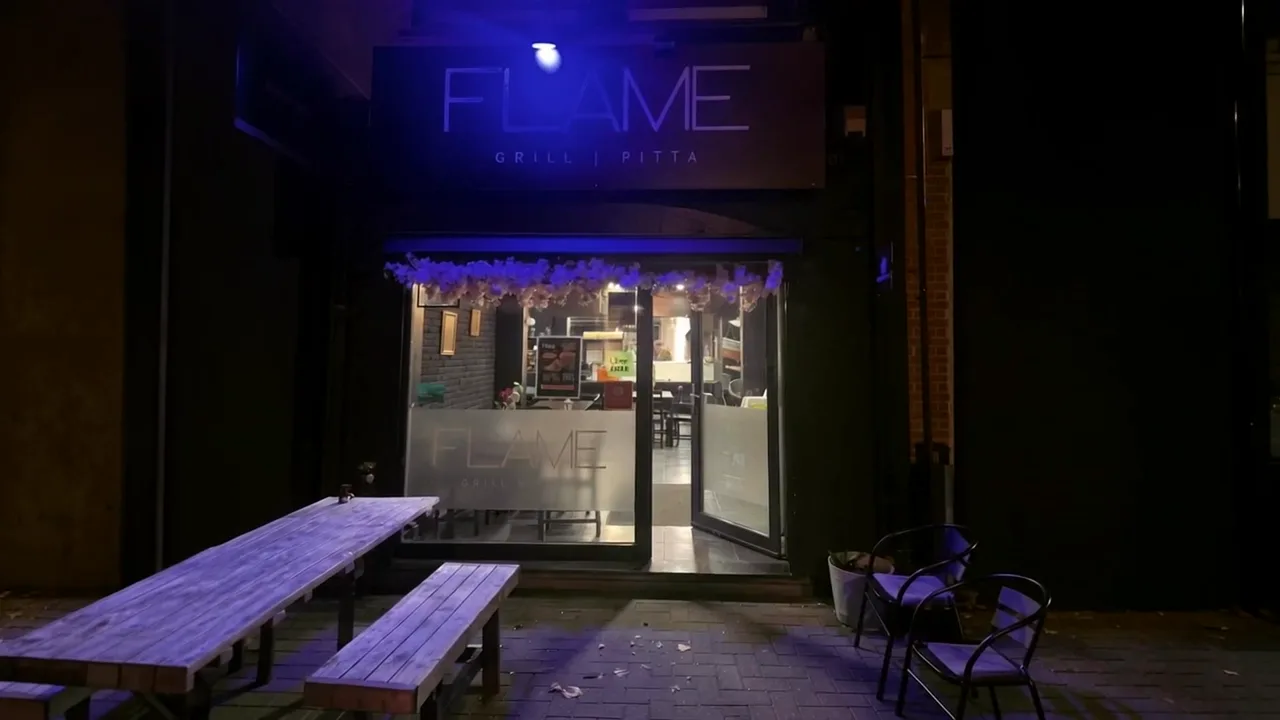 Het interieur van Flame Grill in Gent: kroonluchter, zwarte tafels en de bar met het gouden logo